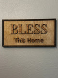 Bless This Home framed wood sign with raised lettering and dark stained frame hanging on wall