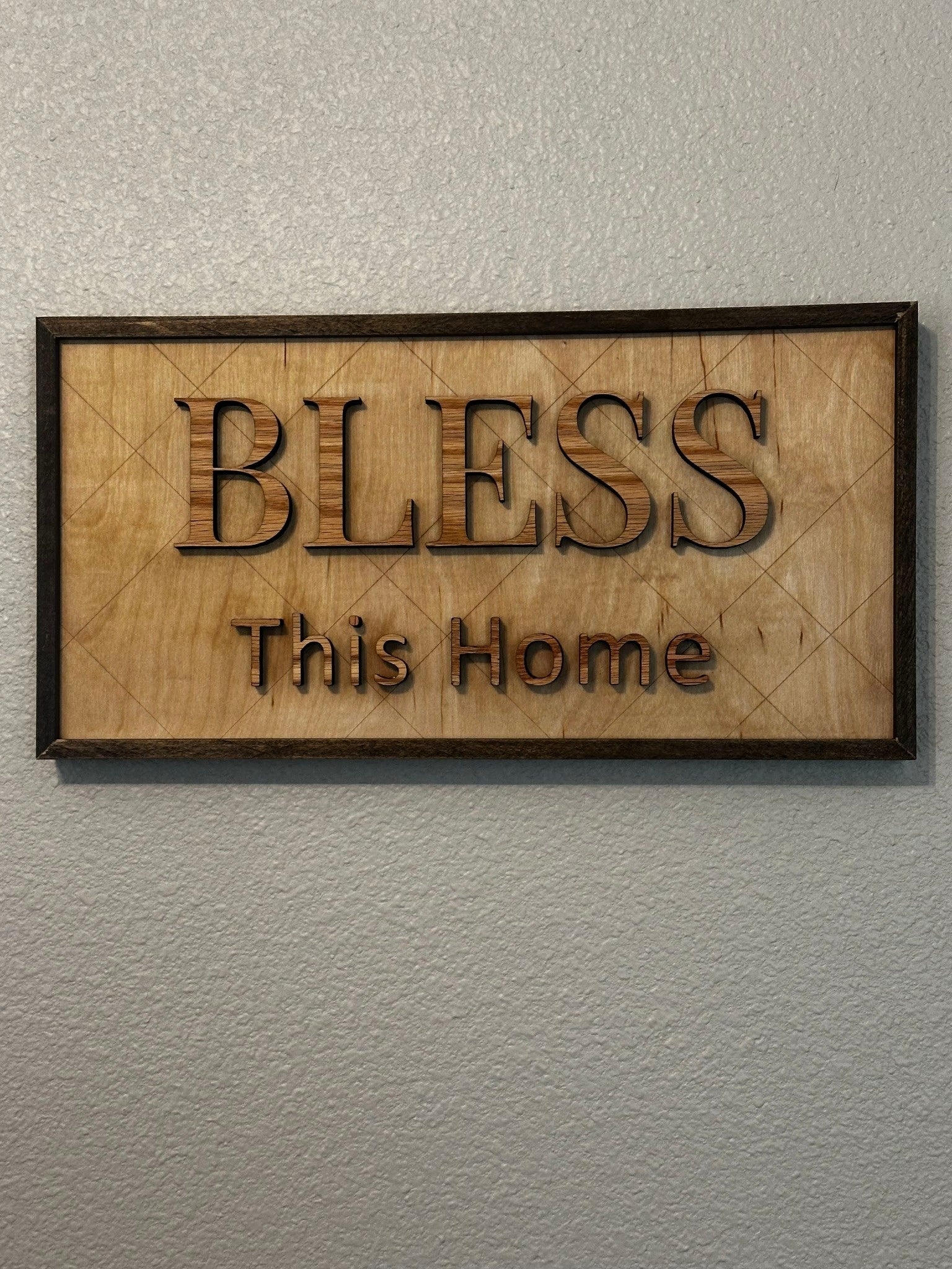 Bless This Home framed wood sign with raised lettering and dark stained frame hanging on wall