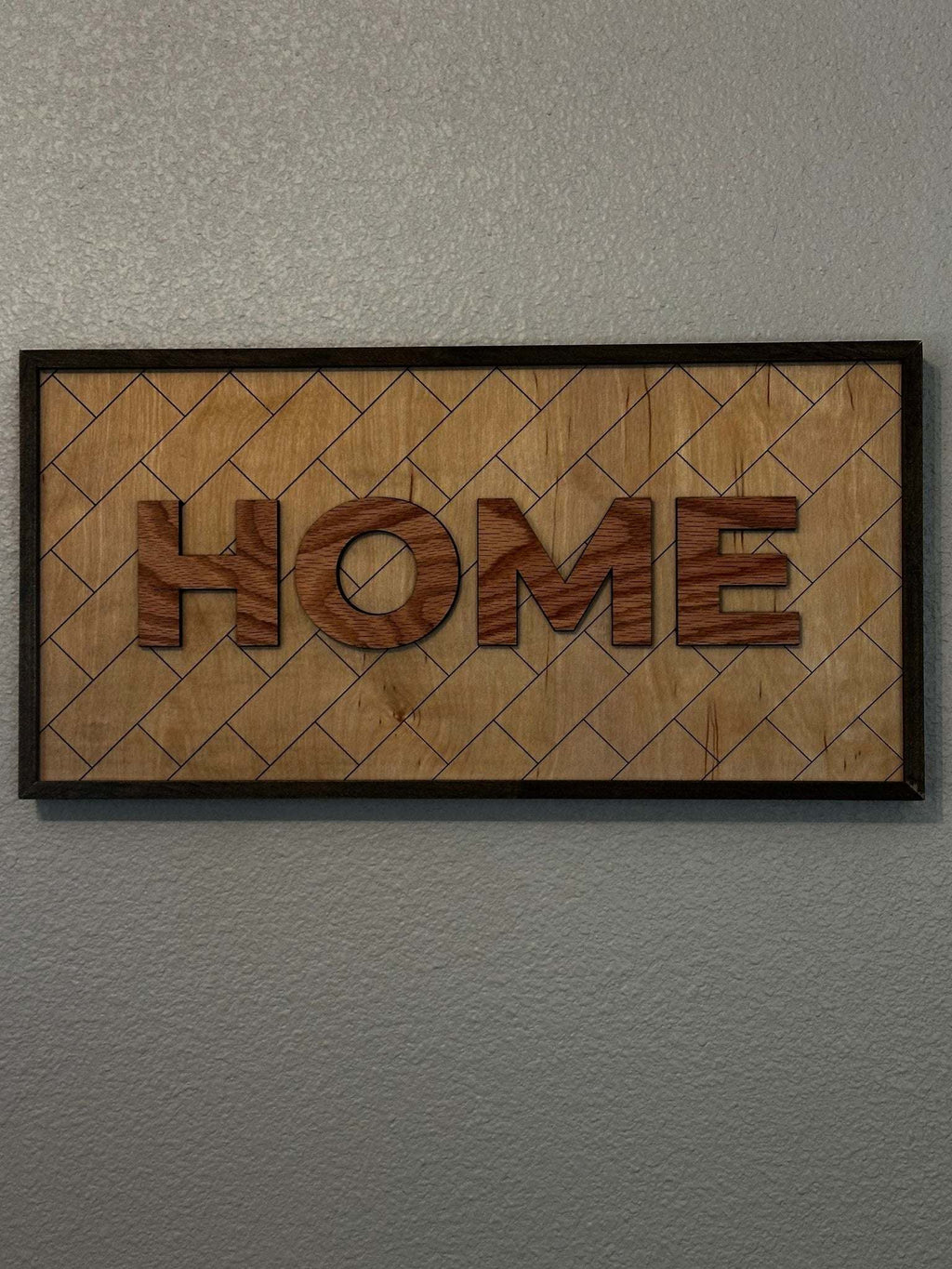 HOME framed wood sign with layered raised letters and laser-engraved geometric background in a dark wood frame.