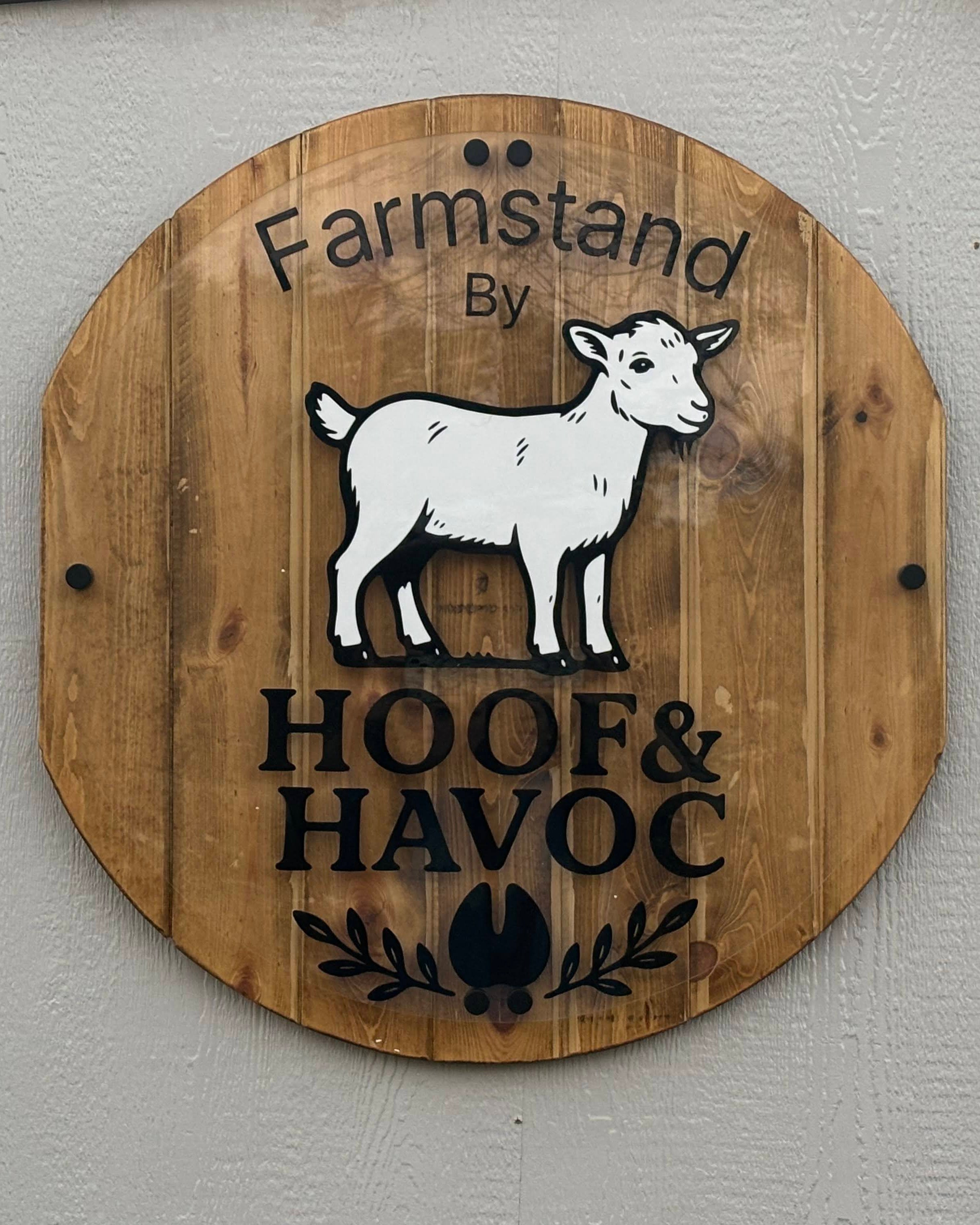 Wooden sign with a goat illustration and 'Farmstand by Hoof & Havoc' text on a gray wall.