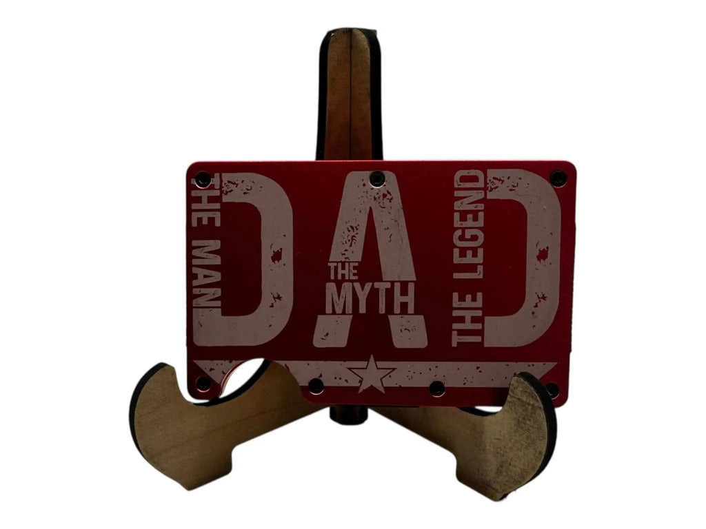Engraved metal money clip wallet in red, featuring "Dad The Man The Myth The Legend" design, displayed on a wooden stand.