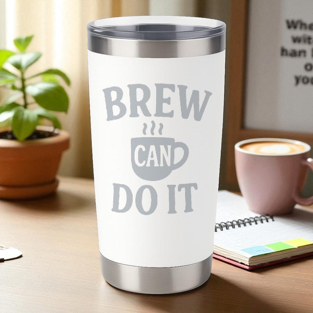 20oz white stainless steel tumbler with engraved "Brew Can Do It" design and clear slide lid on wooden desk with coffee cup and plant background