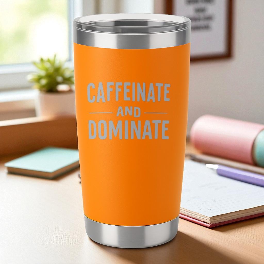 Orange 20oz stainless steel tumbler with "Caffeinate and Dominate" engraved text and clear lid on a desk.