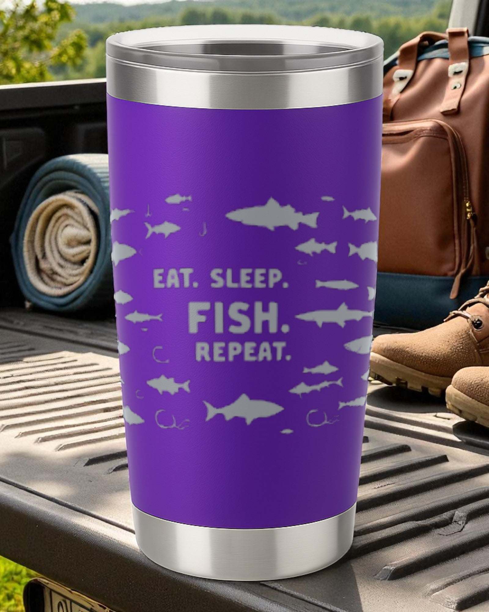 Purple fishing tumbler with "Eat. Sleep. Fish. Repeat." text and fish graphics on outdoor picnic table