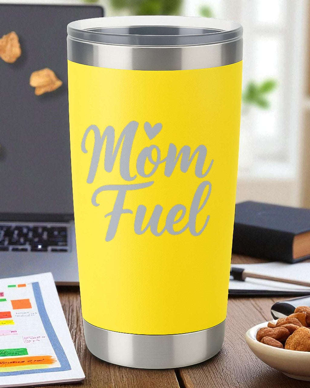 Yellow coffee tumbler with "Mom Fuel" text for coffee-powered moms on a desk with laptop and snacks