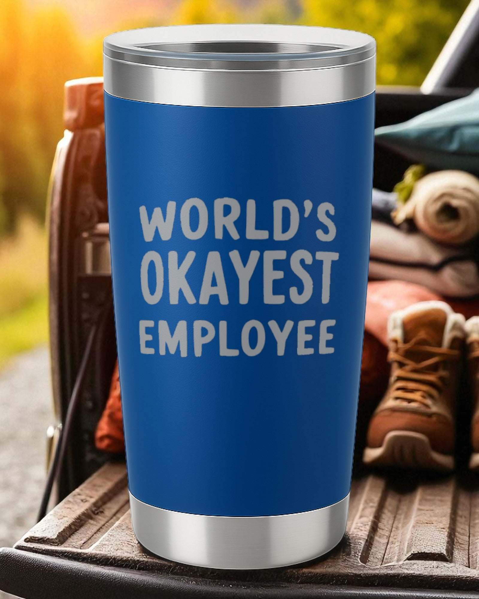 Blue 20oz stainless steel tumbler with "World's Okayest Employee" laser-engraved text and clear sliding lid.